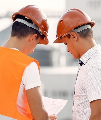 Due ingegneri con i caschi protettivi esaminano le planimetrie in un cantiere edile.