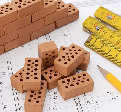 Primo piano di mattoncini in miniatura e metri a nastro su progetti architettonici.